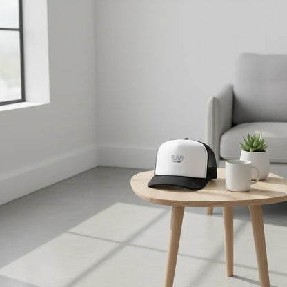 White and black cap on a wooden table in a minimalistic room with a gray sofa and plant.
