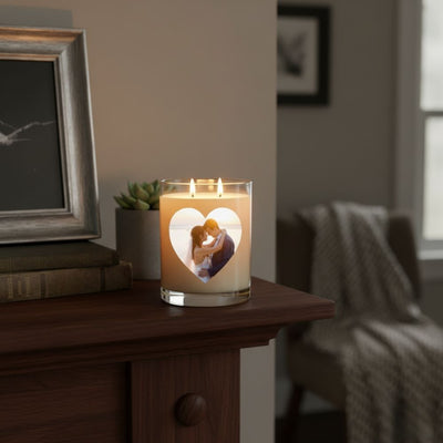 A custom scented candle with a heart-shaped photo of a couple printed on the glass, placed on a wooden mantel beside books and decor in a warm, cozy room.