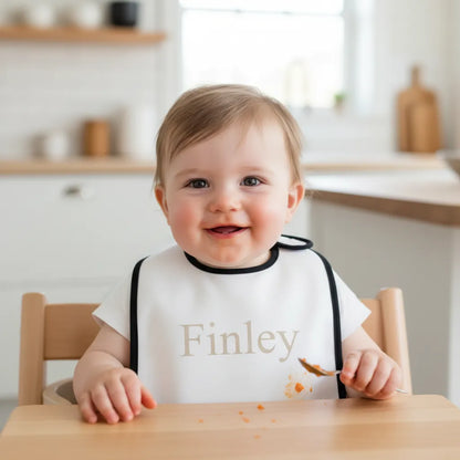 Child wearing a bib with 'Finley' printed on it, sitting at a table in a kitchen.
